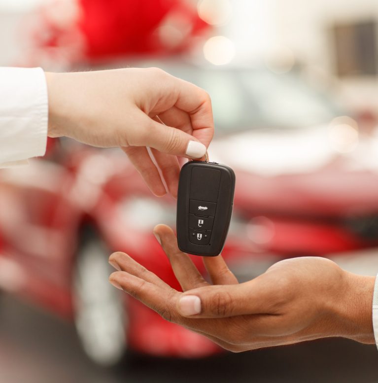 Cropped close up of a male customer receiving car keys from salesperson after buying new automobile at the dealership salon. Car dealer handing key to male customer. Buying car, selling cars concept